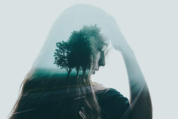 Beautiful and atmospheric double exposure of a girl with her hand to your head, layered with a photo of trees lining a roadway 
