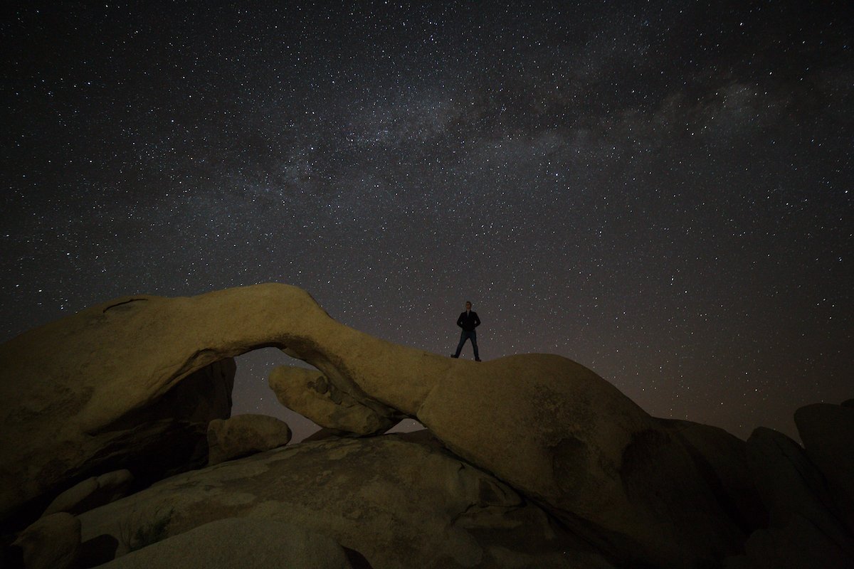 RAW nighttime image of a person standing on a desert formation under the stars