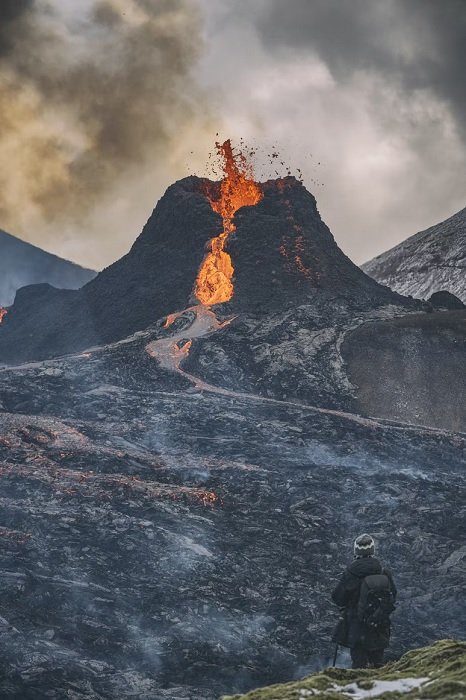 Man in the foreground looking at an erupting volcano