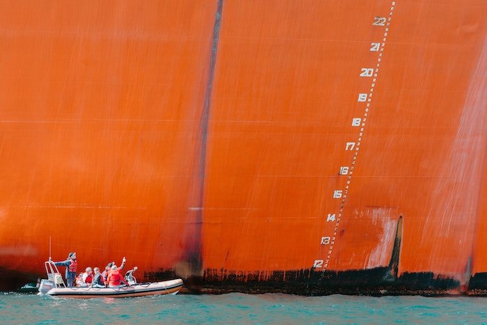 A small boat beside the immense orange-colored side of a large tanker