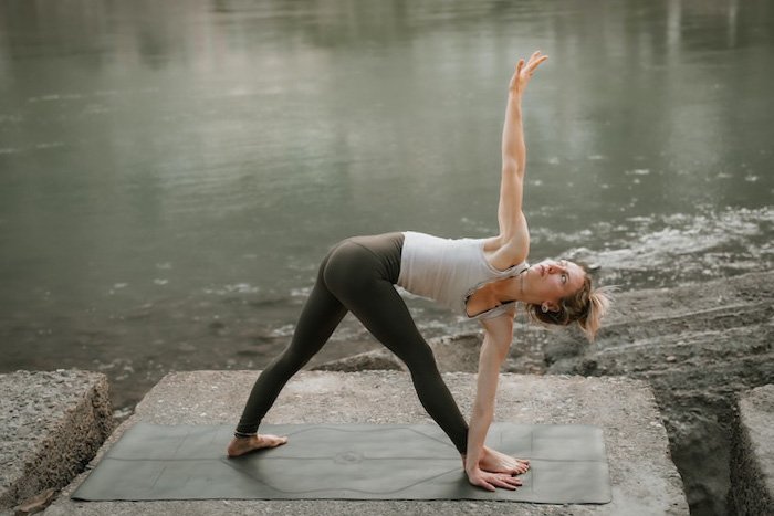A woman doing a yoga triangle pose on a concrete slab by water